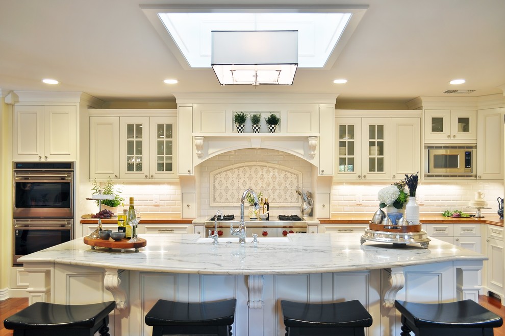 Inspiration for a l-shaped eat-in kitchen in Phoenix with raised-panel cabinets, white cabinets, marble benchtops, white splashback, subway tile splashback and stainless steel appliances.
