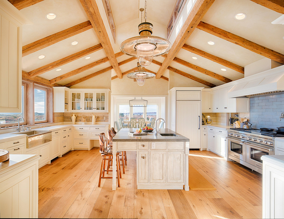 Expansive country u-shaped separate kitchen in Boston with a farmhouse sink, shaker cabinets, white cabinets, blue splashback, stainless steel appliances, medium hardwood floors, with island, brown floor, grey benchtop, solid surface benchtops and porcelain splashback.