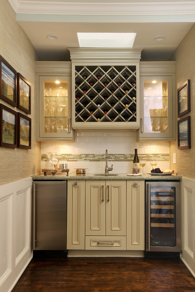Photo of a small traditional single-wall wet bar in Miami with an undermount sink, recessed-panel cabinets, beige cabinets, white splashback, subway tile splashback and dark hardwood floors.