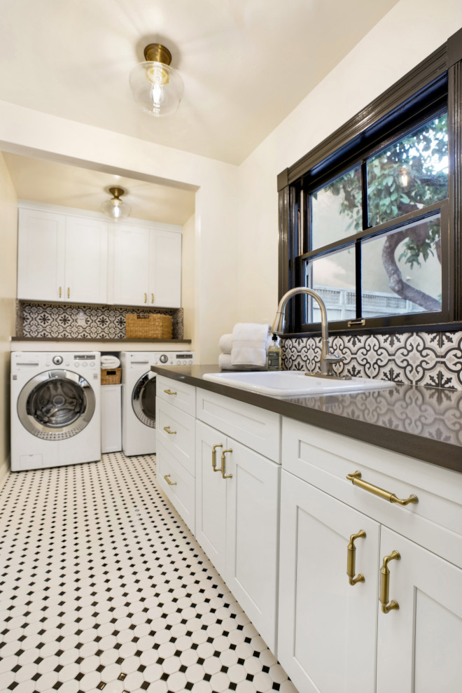 Large transitional l-shaped dedicated laundry room in Orange County with a single-bowl sink, shaker cabinets, white cabinets, quartz benchtops, white splashback, ceramic splashback, white walls, ceramic floors, a side-by-side washer and dryer, white floor and grey benchtop.