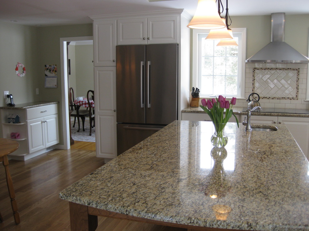 Inspiration for a transitional u-shaped medium tone wood floor eat-in kitchen remodel in Boston with an undermount sink, raised-panel cabinets, white cabinets, granite countertops, white backsplash, ceramic backsplash, stainless steel appliances, an island and beige countertops