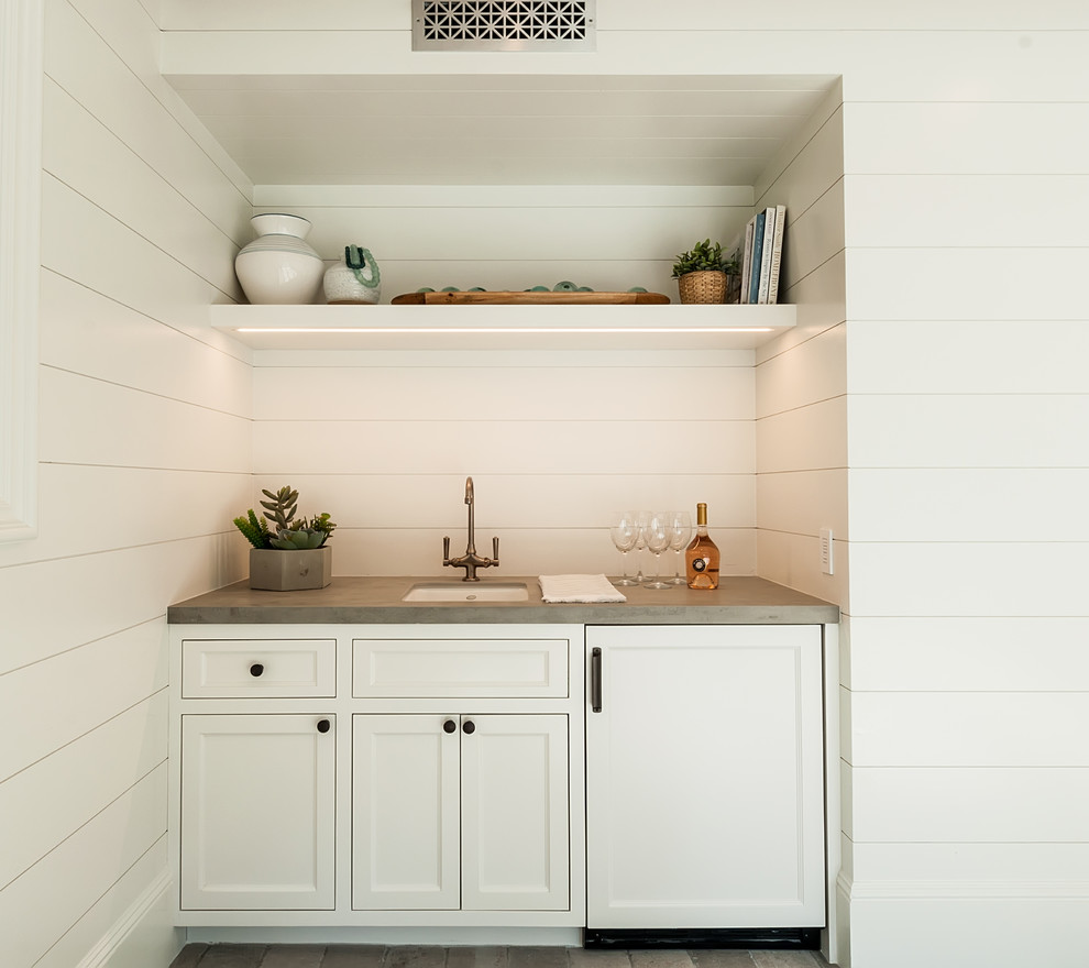 This is an example of a large country single-wall wet bar in Los Angeles with an undermount sink, recessed-panel cabinets, white cabinets, solid surface benchtops, white splashback, limestone floors, grey floor and grey benchtop.