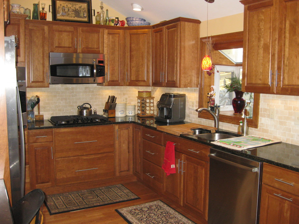 Example of a transitional u-shaped medium tone wood floor eat-in kitchen design in Boston with an undermount sink, raised-panel cabinets, medium tone wood cabinets, granite countertops, beige backsplash, subway tile backsplash, stainless steel appliances, a peninsula and black countertops