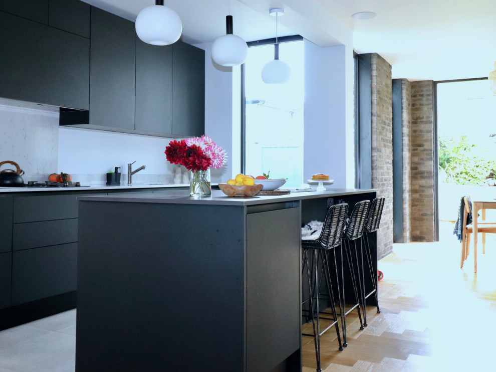 This is an example of a mid-sized arts and crafts single-wall open plan kitchen in London with flat-panel cabinets, grey cabinets, granite benchtops, grey splashback, painted wood floors, with island, multi-coloured benchtop and brown floor.