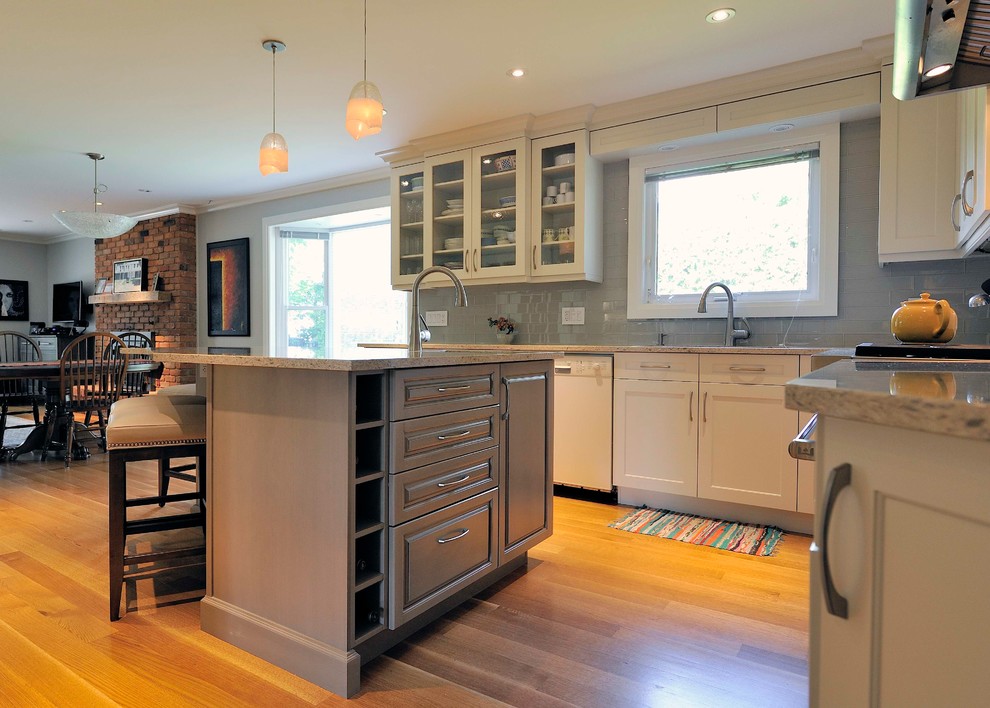 Large transitional l-shaped medium tone wood floor and brown floor open concept kitchen photo in Ottawa with an undermount sink, shaker cabinets, white cabinets, granite countertops, gray backsplash, glass tile backsplash, stainless steel appliances and an island
