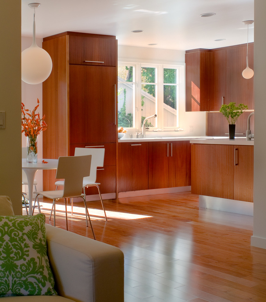 This is an example of a mid-sized contemporary l-shaped open plan kitchen in Los Angeles with a single-bowl sink, flat-panel cabinets, medium wood cabinets, solid surface benchtops, white splashback, ceramic splashback, stainless steel appliances, medium hardwood floors and with island.
