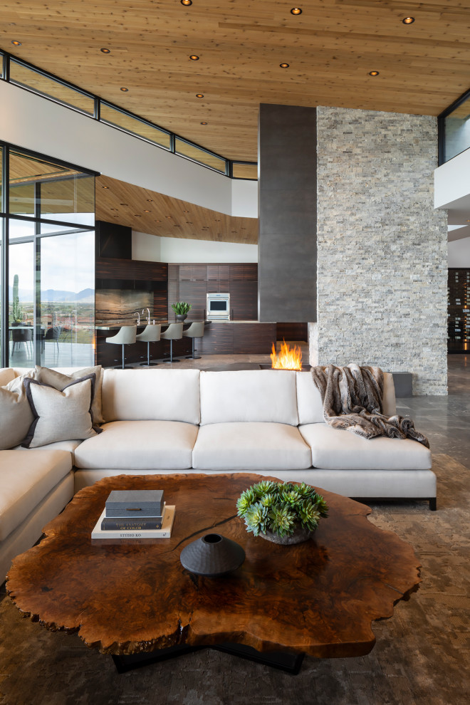 Expansive modern open concept living room in Phoenix with a two-sided fireplace, a stone fireplace surround and wood.