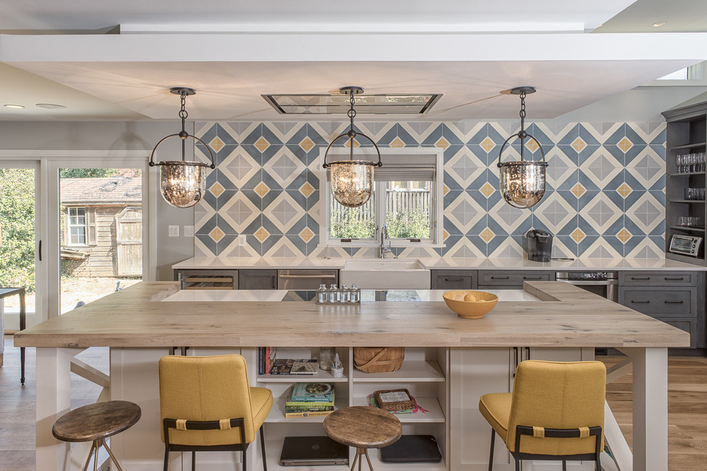 Photo of a large transitional single-wall eat-in kitchen in DC Metro with a farmhouse sink, flat-panel cabinets, grey cabinets, quartz benchtops, grey splashback, cement tile splashback, stainless steel appliances, light hardwood floors and with island.