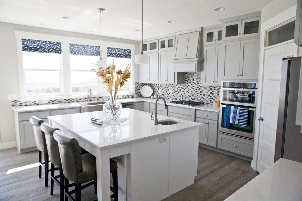 Photo of a beach style u-shaped kitchen in Salt Lake City with an undermount sink, shaker cabinets, grey cabinets, multi-coloured splashback, mosaic tile splashback, stainless steel appliances, dark hardwood floors and with island.