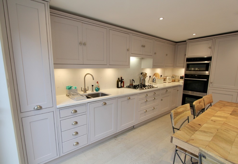 Photo of a mid-sized contemporary single-wall eat-in kitchen in London with a drop-in sink, shaker cabinets, purple cabinets, solid surface benchtops, white splashback, stainless steel appliances, medium hardwood floors, no island, brown floor and white benchtop.