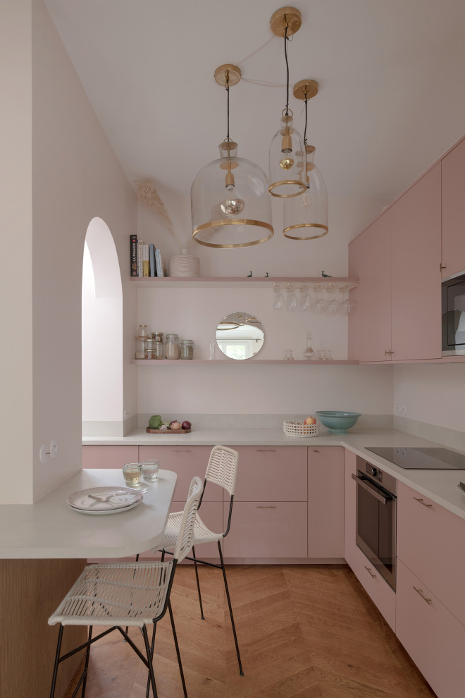 Idées déco pour cuisine en L avec un placard à porte plane, des portes de placard rose, un électroménager en acier inoxydable, un sol en bois brun, une péninsule, un sol marron et un plan de travail blanc.
