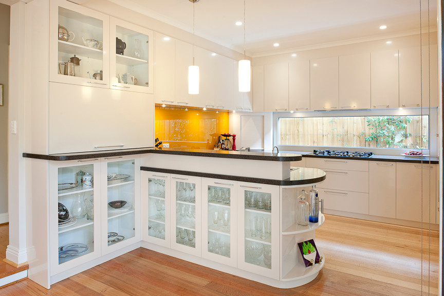 Inspiration for a mid-sized traditional u-shaped eat-in kitchen in Melbourne with a peninsula, recessed-panel cabinets, white cabinets, quartz benchtops, orange splashback, glass sheet splashback, stainless steel appliances, a double-bowl sink and light hardwood floors.