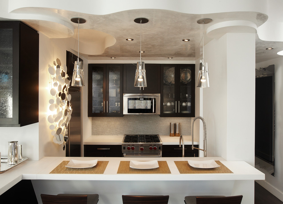 This is an example of a small contemporary galley open plan kitchen in New York with glass-front cabinets, black cabinets, stainless steel appliances, dark hardwood floors, no island, an undermount sink, solid surface benchtops, white splashback and matchstick tile splashback.