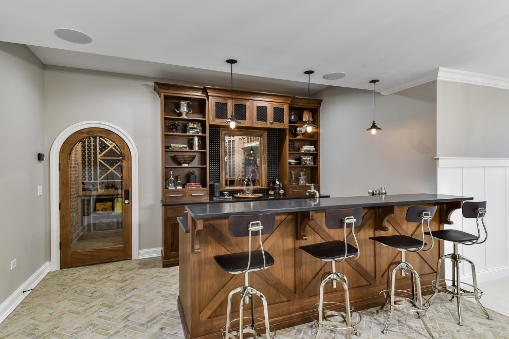 Photo of a large traditional l-shaped wet bar in Chicago with an undermount sink, recessed-panel cabinets, medium wood cabinets, quartzite benchtops, grey splashback, ceramic splashback, brick floors, brown floor and grey benchtop.