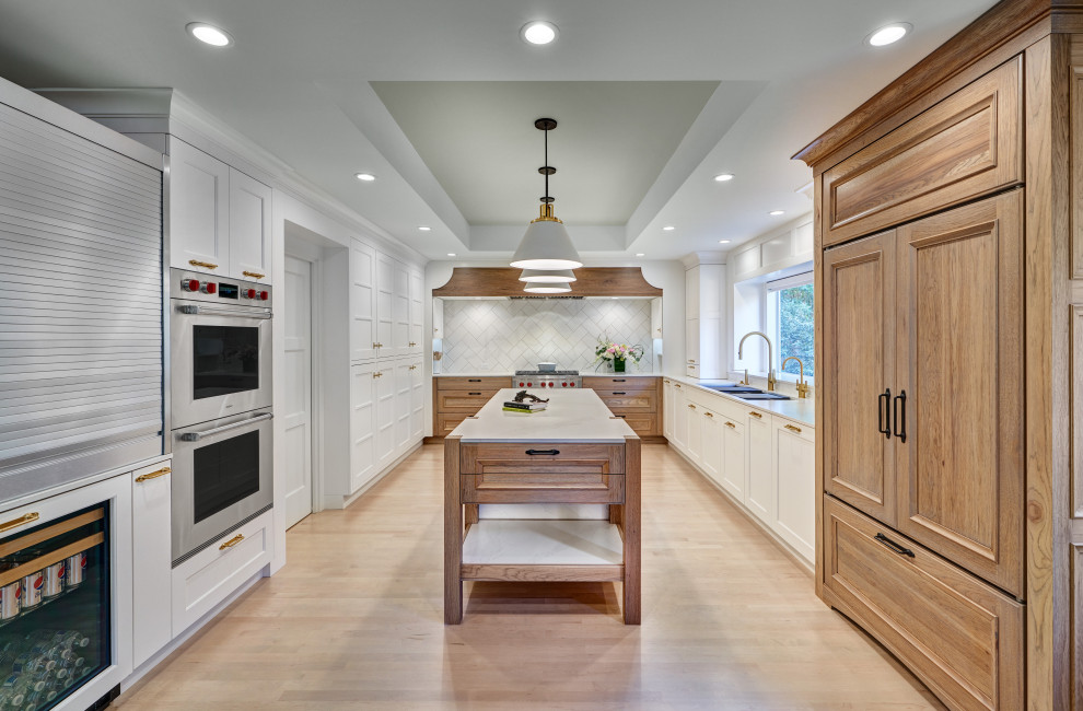 Inspiration for a large u-shaped open plan kitchen in Sacramento with shaker cabinets, an island, a submerged sink, white cabinets, engineered stone countertops, white splashback, stone tiled splashback, stainless steel appliances, light hardwood flooring, brown floors, white worktops, a drop ceiling and a feature wall.