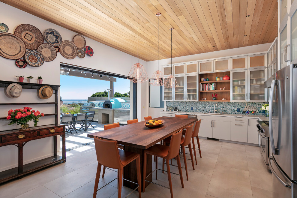 Design ideas for a mid-sized beach style u-shaped open plan kitchen in Santa Barbara with an undermount sink, flat-panel cabinets, stainless steel cabinets, quartzite benchtops, multi-coloured splashback, glass tile splashback, stainless steel appliances, porcelain floors, no island, beige floor, white benchtop and wood.