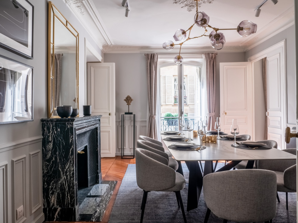 Photo of a mid-sized transitional separate dining room in Paris with grey walls, dark hardwood floors and a standard fireplace.