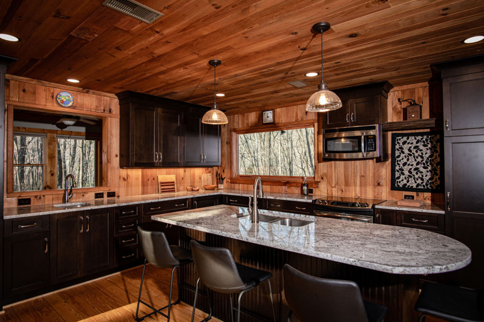 This is an example of a mid-sized country l-shaped eat-in kitchen in Other with an undermount sink, flat-panel cabinets, dark wood cabinets, granite benchtops, timber splashback, stainless steel appliances, medium hardwood floors, with island, white benchtop and wood.