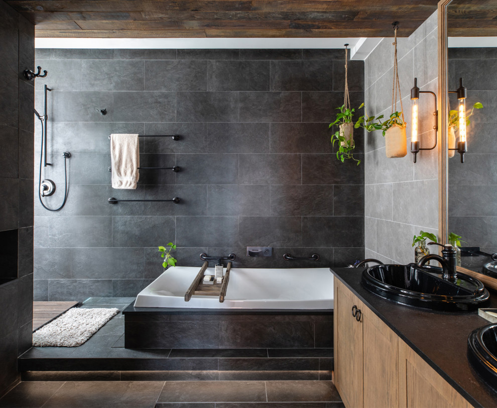 Inspiration for an industrial bathroom in Hong Kong with shaker cabinets, medium wood cabinets, a drop-in tub, gray tile, a drop-in sink, grey floor and black benchtops.