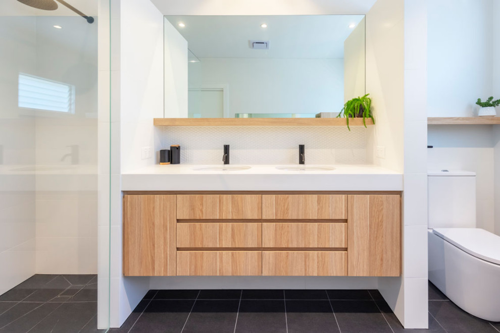Inspiration for a contemporary kids bathroom in Sydney with furniture-like cabinets, medium wood cabinets, a freestanding tub, an open shower, a one-piece toilet, white tile, mosaic tile, white walls, porcelain floors, an undermount sink, engineered quartz benchtops, black floor, an open shower and white benchtops.