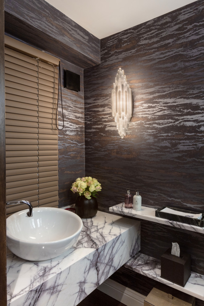 Foto på ett litet funkis vit badrum, med vita skåp, en vägghängd toalettstol, lila väggar, mellanmörkt trägolv, ett fristående handfat, marmorbänkskiva och brunt golv