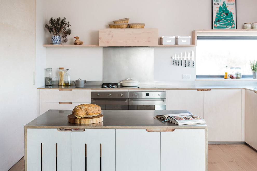 Inspiration for a mid-sized scandinavian l-shaped eat-in kitchen in Other with a farmhouse sink, flat-panel cabinets, light wood cabinets, stainless steel benchtops, metallic splashback, stainless steel appliances, light hardwood floors and with island.