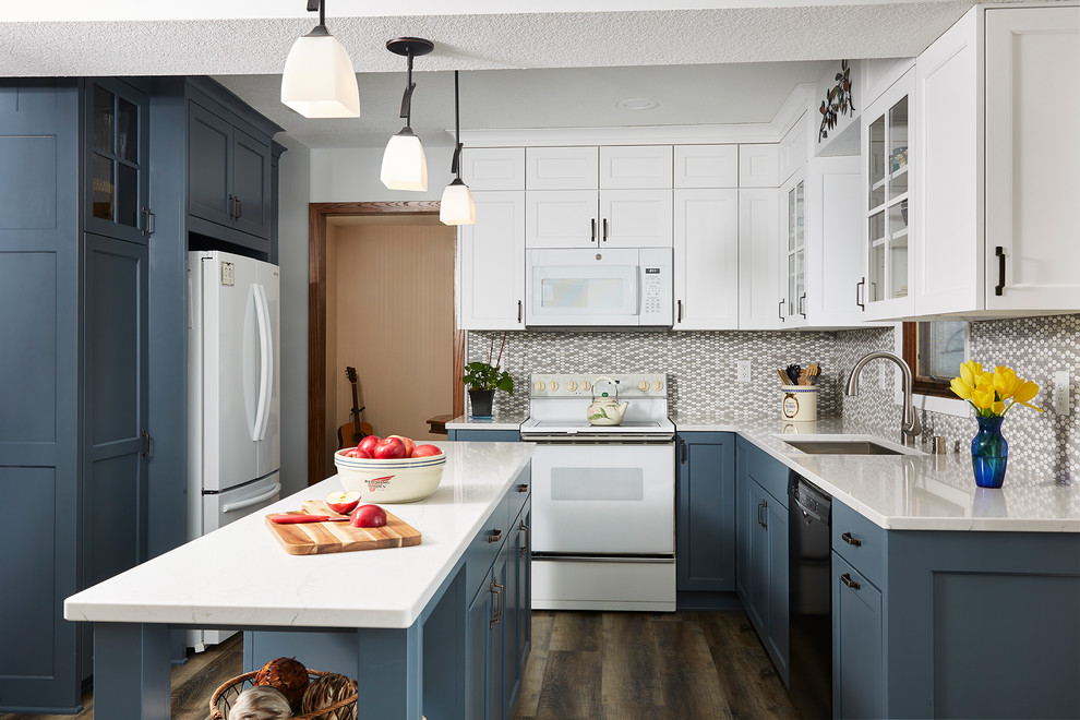This is an example of a large transitional u-shaped kitchen in Minneapolis with an undermount sink, shaker cabinets, blue cabinets, grey splashback, mosaic tile splashback, white appliances, dark hardwood floors, with island, brown floor and white benchtop.