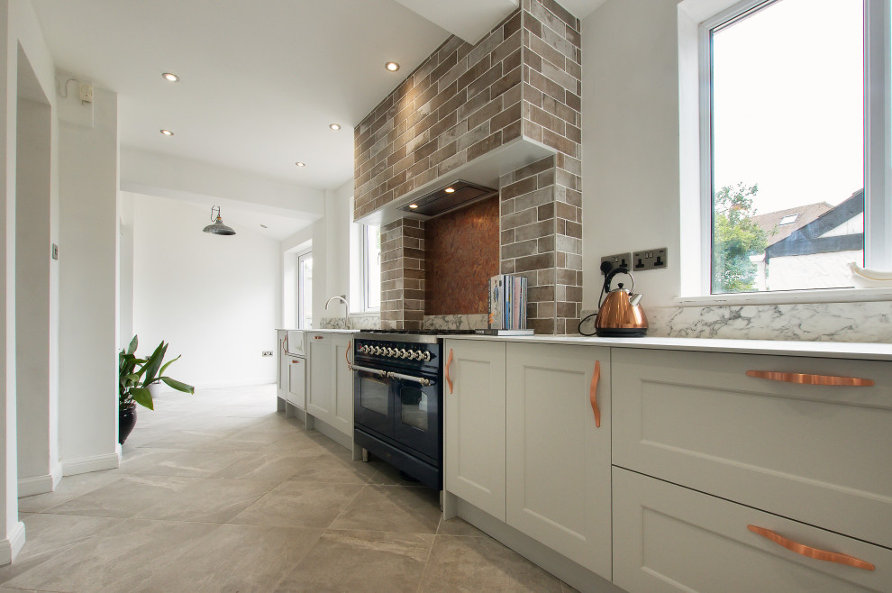 Photo of a medium sized classic grey and white l-shaped enclosed kitchen in Cardiff with a belfast sink, shaker cabinets, grey cabinets, marble worktops, metallic splashback, metal splashback, stainless steel appliances, porcelain flooring, no island, grey floors, white worktops and a chimney breast.