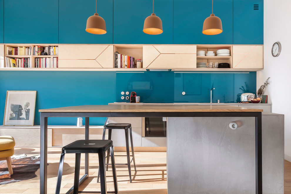 Design ideas for a mid-sized contemporary galley open plan kitchen in Paris with a single-bowl sink, beaded inset cabinets, light wood cabinets, concrete benchtops, glass sheet splashback, panelled appliances, light hardwood floors, with island, blue splashback and grey benchtop.