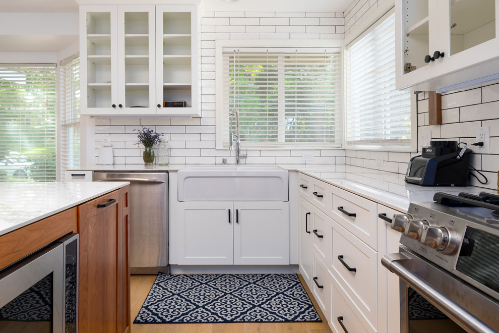 Open concept kitchen - transitional l-shaped light wood floor and beige floor open concept kitchen idea with a farmhouse sink, white cabinets, quartz countertops, white backsplash, subway tile backsplash, stainless steel appliances, an island and white countertops