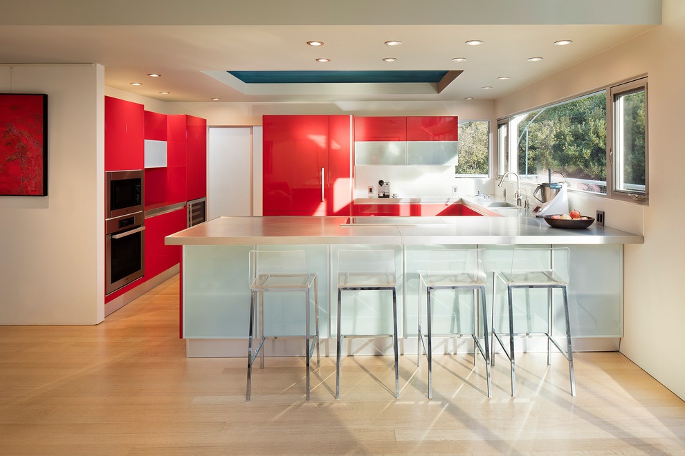 Inspiration for a mid-sized contemporary u-shaped kitchen in San Francisco with a single-bowl sink, flat-panel cabinets, red cabinets, stainless steel benchtops, white splashback, glass sheet splashback, stainless steel appliances, light hardwood floors, a peninsula, grey benchtop and beige floor.