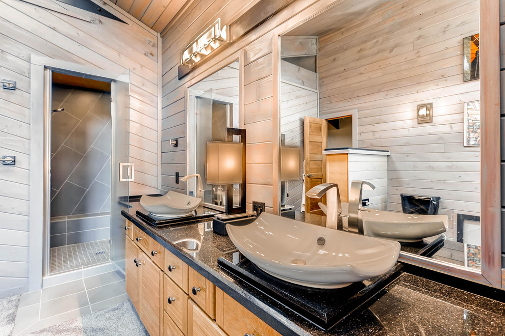 Corner shower - mid-sized rustic master black tile and cement tile concrete floor corner shower idea in Denver with flat-panel cabinets, light wood cabinets, a one-piece toilet, brown walls, a vessel sink and quartzite countertops