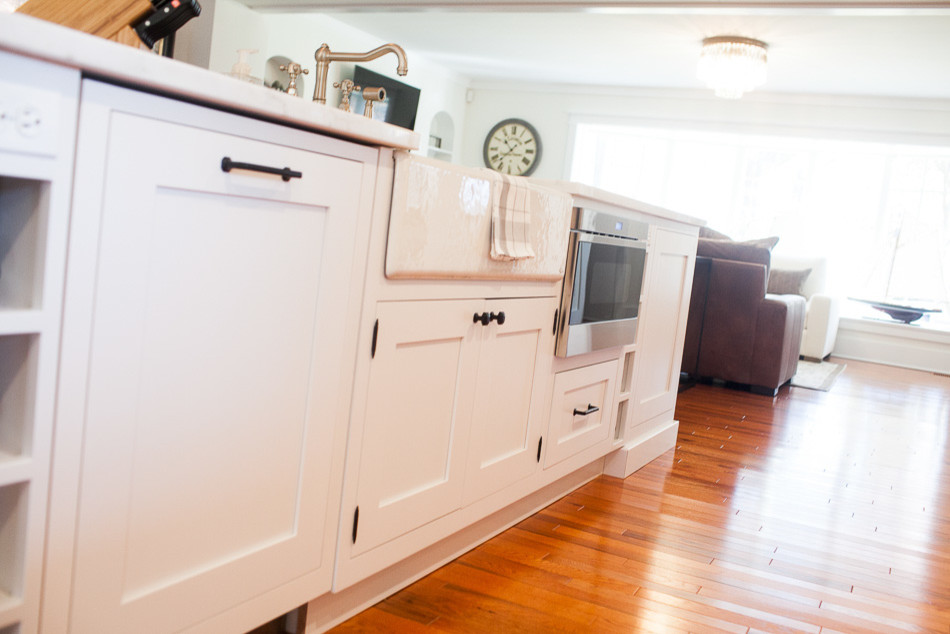 Inspiration for a mid-sized transitional medium tone wood floor eat-in kitchen remodel in St Louis with a farmhouse sink, flat-panel cabinets, white cabinets, white backsplash, subway tile backsplash, stainless steel appliances and an island
