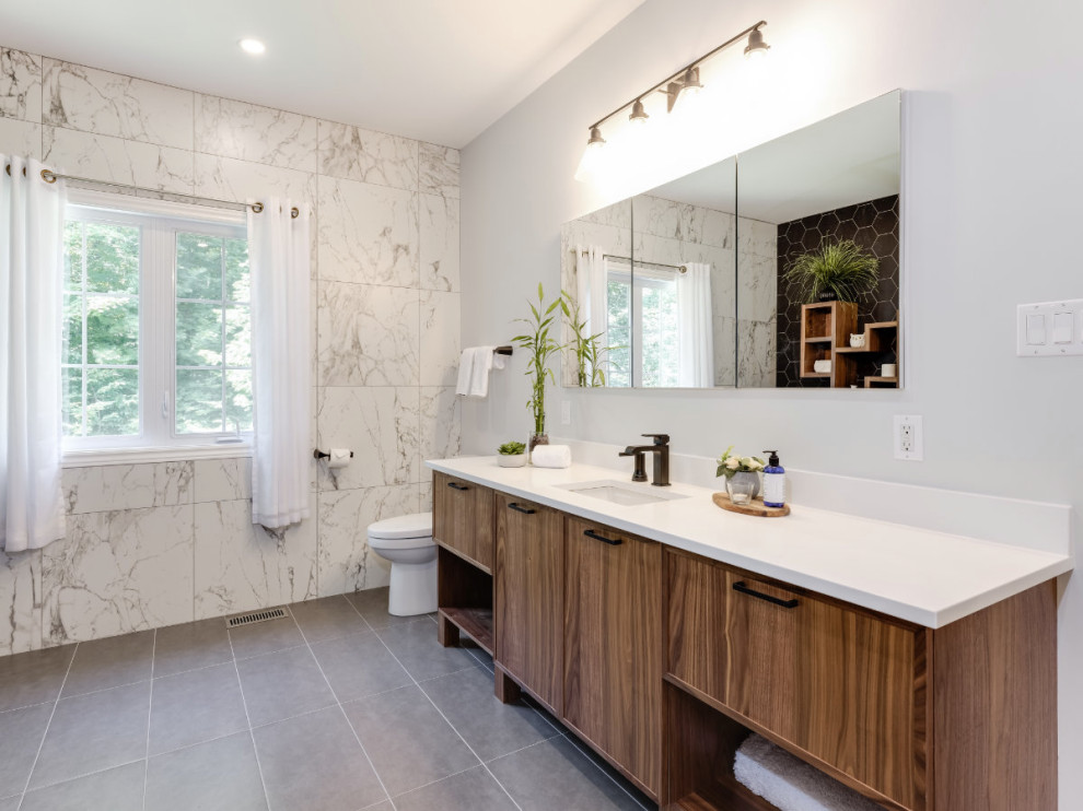 Inspiration for a large contemporary ensuite bathroom in Ottawa with flat-panel cabinets, medium wood cabinets, a freestanding bath, a corner shower, porcelain tiles, porcelain flooring, a submerged sink, engineered stone worktops, grey floors, a hinged door, white worktops, a shower bench, a single sink and a freestanding vanity unit.