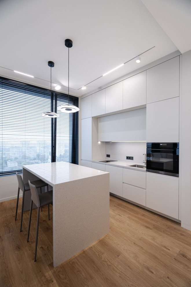 This is an example of a medium sized contemporary galley kitchen/diner in Other with a single-bowl sink, flat-panel cabinets, grey cabinets, composite countertops, grey splashback, integrated appliances, dark hardwood flooring, an island, brown floors, grey worktops and feature lighting.