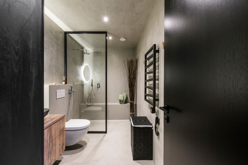 This is an example of a contemporary wet room bathroom in Lyon with flat-panel cabinets, brown cabinets, a wall-mount toilet, cement tile, grey walls, concrete floors, a wall-mount sink, wood benchtops, grey floor and an open shower.