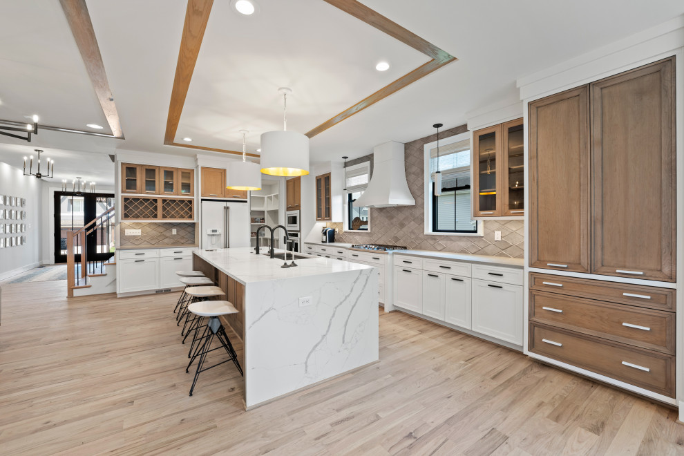 Inredning av ett modernt stort flerfärgad flerfärgat kök, med en trippel diskho, luckor med profilerade fronter, skåp i ljust trä, bänkskiva i kvarts, grått stänkskydd, stänkskydd i keramik, vita vitvaror, ljust trägolv, en köksö och beiget golv