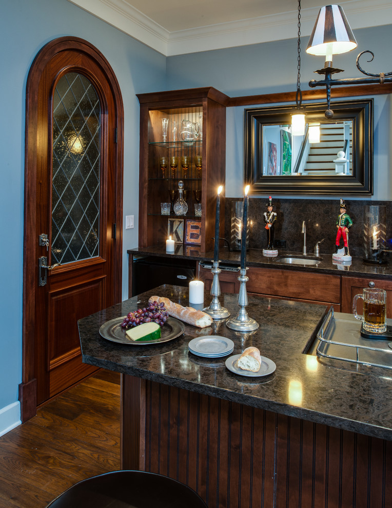 Photo of a traditional home bar in Detroit with an undermount sink, shaker cabinets, dark wood cabinets, black splashback, stone slab splashback, dark hardwood floors and black benchtop.