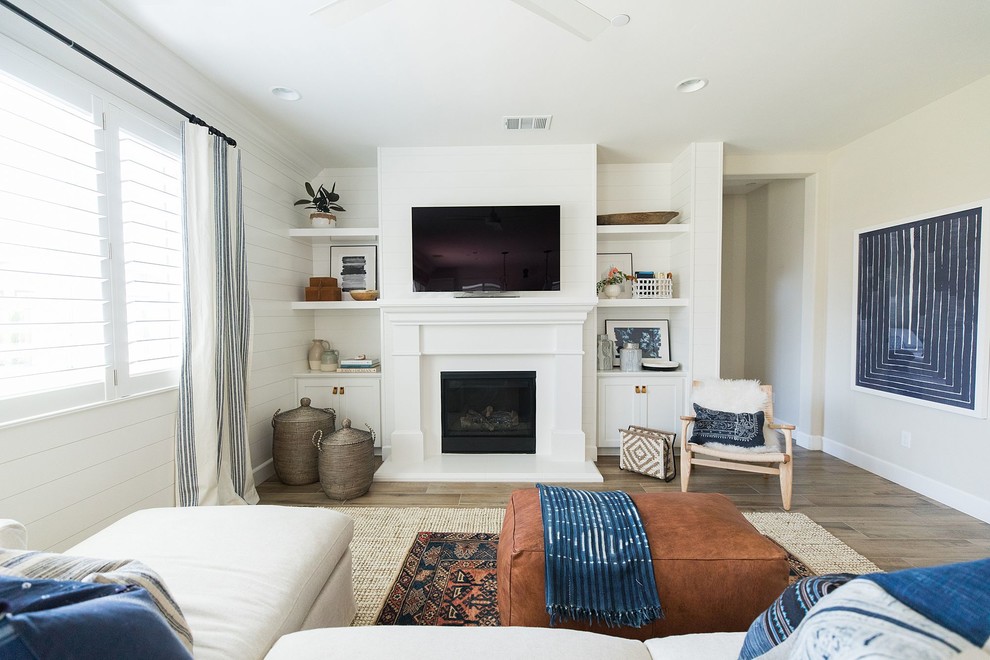 Inspiration for a beach style family room in Sacramento with white walls, a standard fireplace, a wall-mounted tv and brown floor.