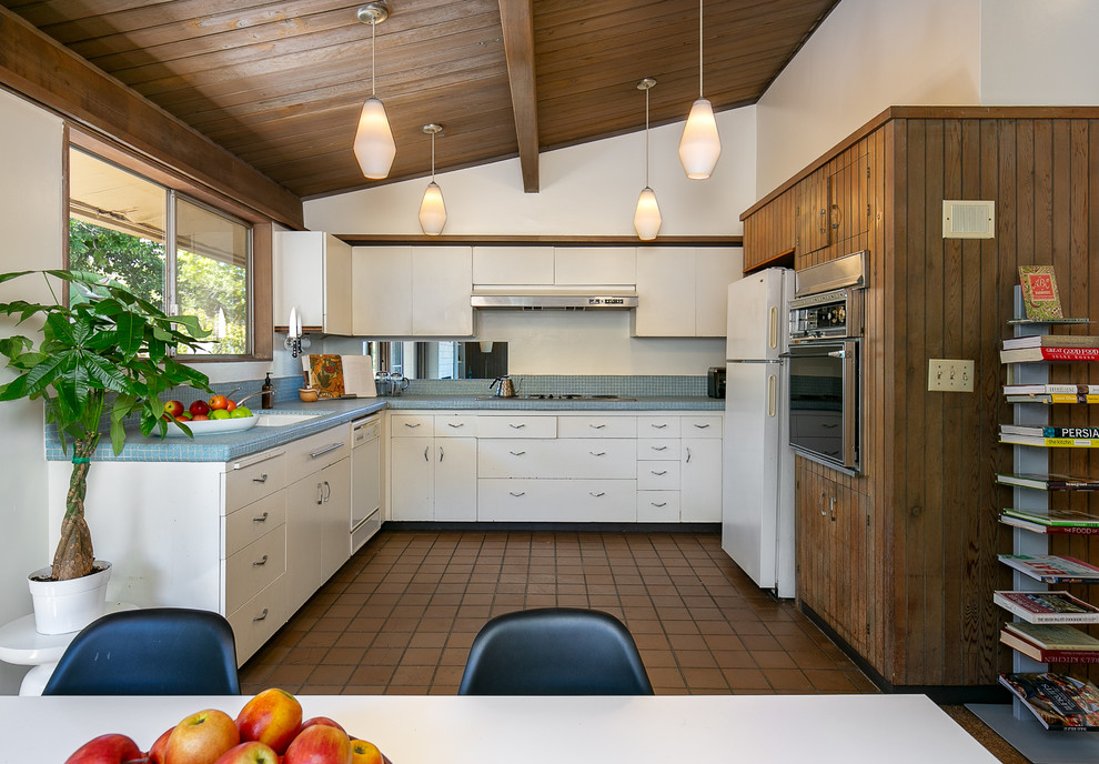 Inspiration for a midcentury u-shaped eat-in kitchen in Los Angeles with an undermount sink, flat-panel cabinets, white cabinets, tile benchtops, blue splashback, mosaic tile splashback, white appliances, no island, brown floor and blue benchtop.