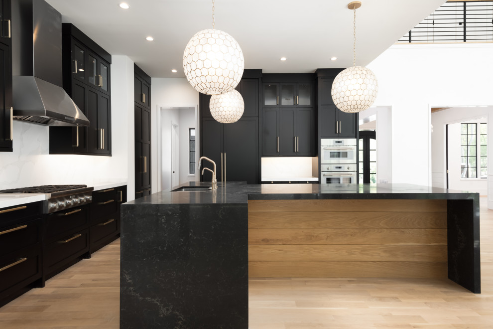 Mid-sized transitional u-shaped light wood floor kitchen photo with an undermount sink, shaker cabinets, black cabinets, quartz countertops, white backsplash, quartz backsplash, stainless steel appliances, an island and black countertops
