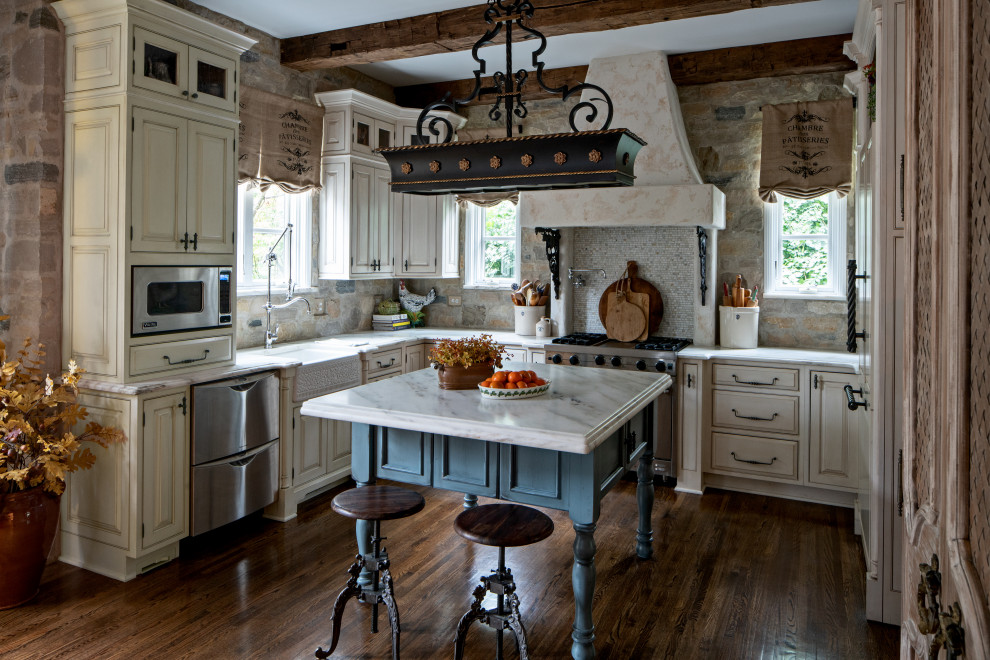 Large french country u-shaped dark wood floor, brown floor and exposed beam open concept kitchen photo in Chicago with a farmhouse sink, raised-panel cabinets, beige cabinets, marble countertops, multicolored backsplash, stone slab backsplash, stainless steel appliances, an island and white countertops