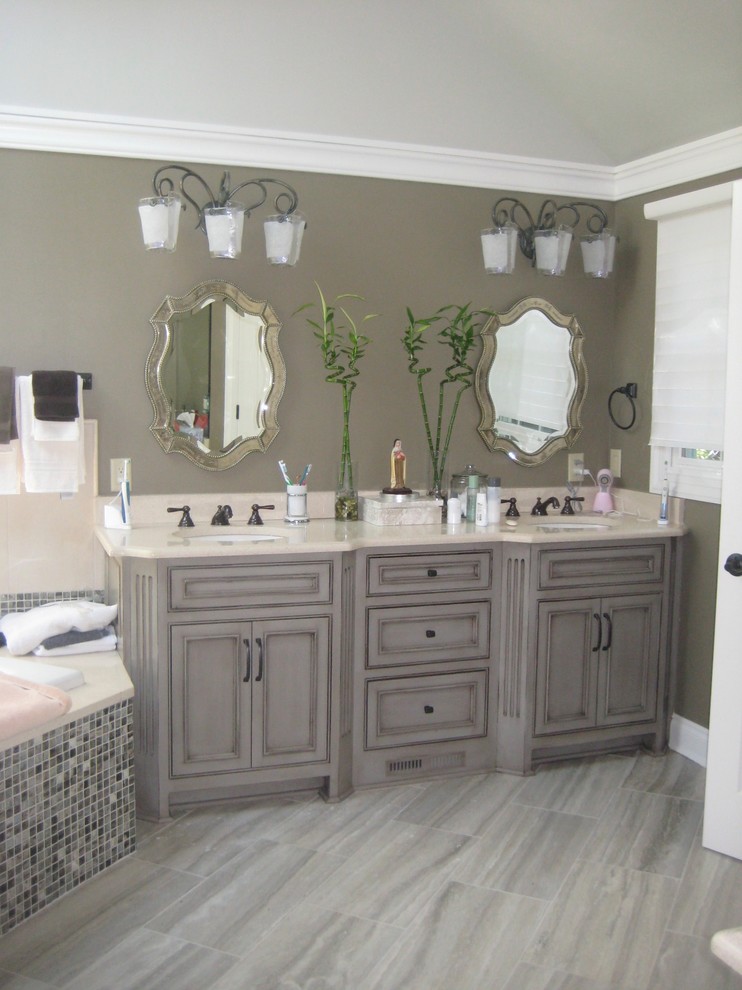 This is an example of a mid-sized traditional master bathroom in Cleveland with beaded inset cabinets, grey cabinets, a drop-in tub, a corner shower, beige tile, stone slab, solid surface benchtops, a hinged shower door, a two-piece toilet, brown walls, porcelain floors, an undermount sink and brown floor.