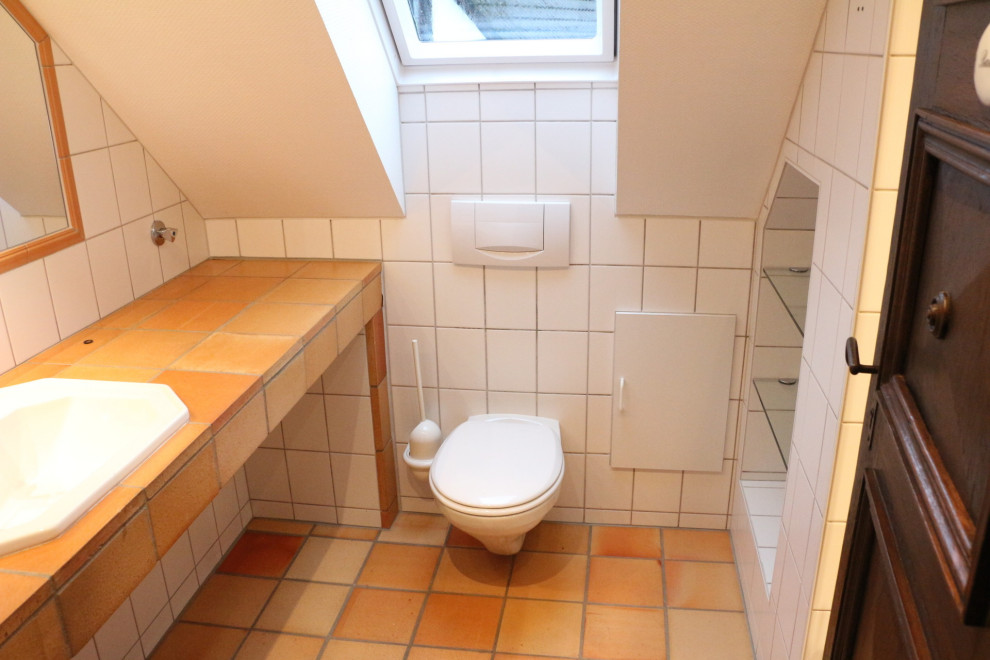 Foto på ett litet lantligt orange toalett, med orange skåp, en toalettstol med separat cisternkåpa, vit kakel, keramikplattor, vita väggar, klinkergolv i terrakotta, ett integrerad handfat, kaklad bänkskiva och orange golv