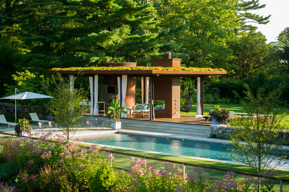 Photo of a large contemporary backyard rectangular lap pool in New York with a pool house and natural stone pavers.