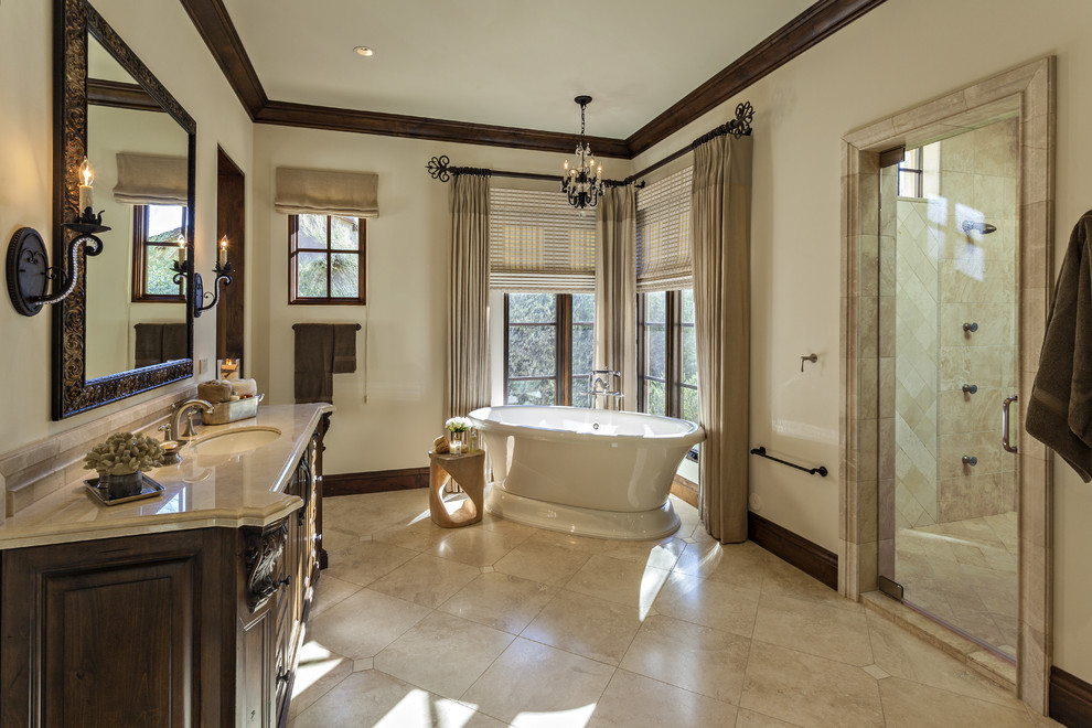 Design ideas for a large mediterranean master bathroom in Phoenix with furniture-like cabinets, brown cabinets, a freestanding tub, a double shower, beige tile, marble, white walls, travertine floors, an undermount sink, marble benchtops, beige floor, a hinged shower door, a one-piece toilet and beige benchtops.