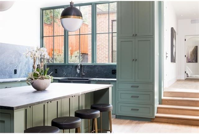 Example of a large transitional single-wall medium tone wood floor and beige floor eat-in kitchen design in Austin with a farmhouse sink, shaker cabinets, green cabinets, soapstone countertops, black backsplash, stone slab backsplash, colored appliances, an island and black countertops