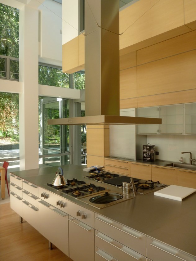 Example of a mid-sized u-shaped light wood floor eat-in kitchen design with a single-bowl sink, flat-panel cabinets, light wood cabinets, stainless steel countertops, white backsplash, subway tile backsplash, stainless steel appliances and an island