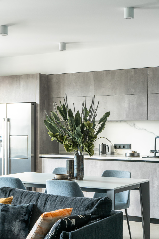Photo of a large contemporary single-wall eat-in kitchen in Other with a drop-in sink, flat-panel cabinets, grey cabinets, tile benchtops, white splashback, porcelain splashback, stainless steel appliances, porcelain floors, no island, grey floor and white benchtop.