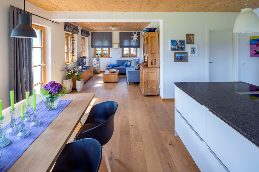 Offenes Country Wohnzimmer mit weißer Wandfarbe, braunem Holzboden, braunem Boden und Holzdecke in München